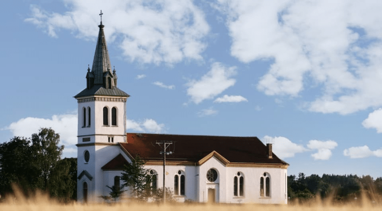 white church with wheat in front trees in back blue sky